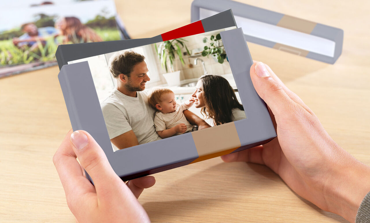 Una persona feliz sostiene un libro de fotos cuidadosamente diseñado. En la portada, una familia sonriente. El ambiente es cálido.