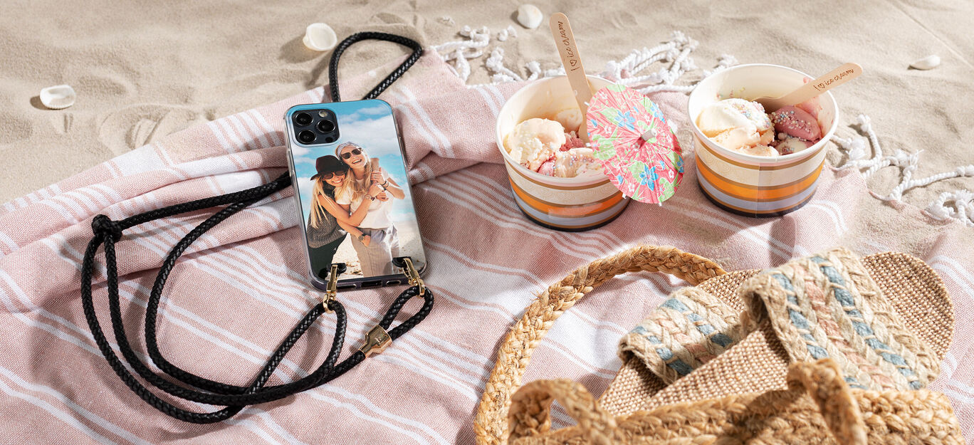 Un smartphone con una funda personalizada se relaja junto a dos cuencos de helado en la playa.