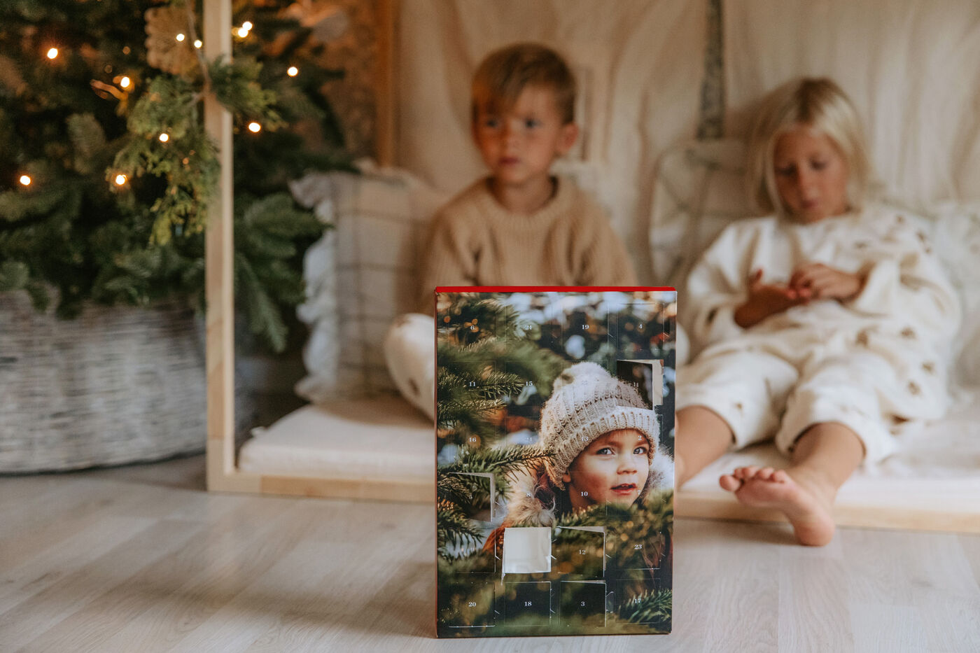 Niños sentados junto a un árbol de Navidad y un calendario de Adviento personalizado en primer plano.