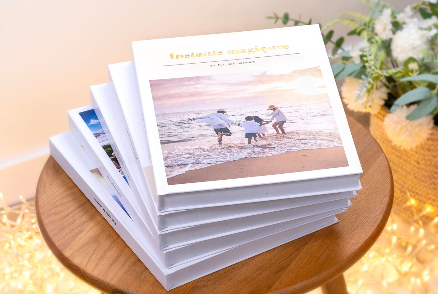 Pila de varios álbumes de fotos de tapa dura sobre una mesa de madera redonda. El álbum superior muestra en su portada una foto de familia.