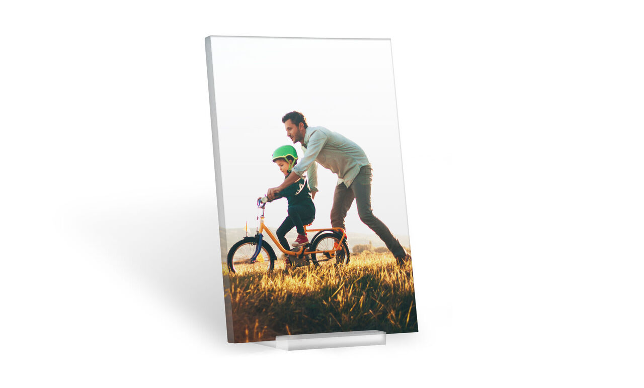 Un padre feliz empuja a su hijo en una bicicleta colorida por un campo soleado. Ambos usan cascos y disfrutan juntos.