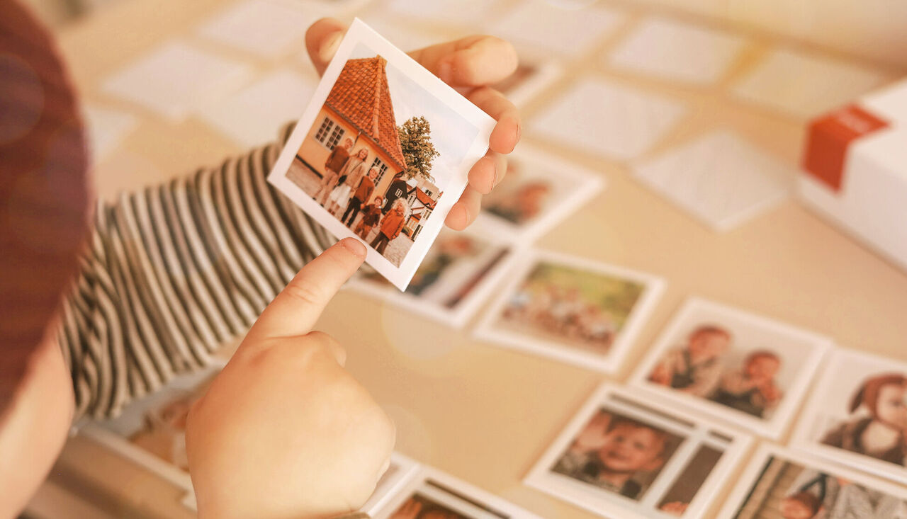 Un niño señala una foto de una familia frente a una hermosa casa en una colección de imágenes.