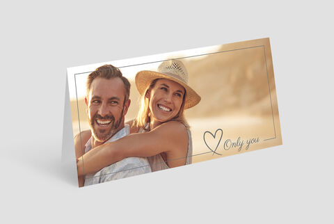 Dos personas abrazándose al aire libre, con sombrero de sol, fondo de playa.